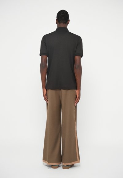 Μαύρο πόλο μπλουζάκι με κοντά μανίκια σε συνδυασμό με καφέ παντελόνι φαρδιάς γραμμής που διαθέτει αντίθετη ρίγα στο πλάι. Μινιμαλιστικός σχεδιασμός, μονοχρωμίες.