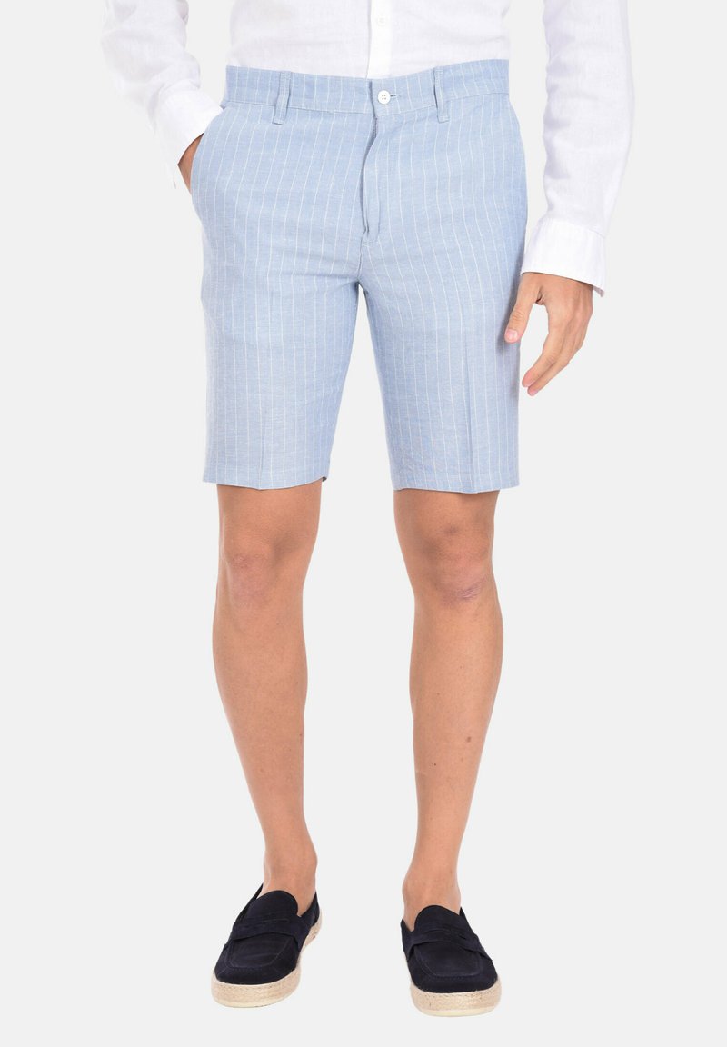 Pantaloni corta a righe blu chiaro realizzati in tessuto leggero, dotati di due tasche frontali e una vestibilità sartoriale, abbinati a scarpe scamosciate scure senza lacci.