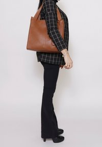 Bruine leren tote bag met een gestructureerde afwerking en dubbele handvatten, met een rechthoekige vorm, zijvak en een minimalistisch ontwerp.