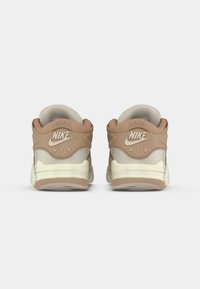 Nike Air Sneaker in einer beige- und cremfarbenen Farbgebung. Ausgestattet mit einem glatten Lederobermaterial, gepolstertem Kragen und sichtbarer Luftdämpfung in der Sohle.