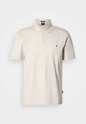 Beež puuvillane polo-särk klassikalise krae, kolme nupuga esikinnitus ja vasakul rinnal väikese tikitud logoga. Lühikeste varrukatega.