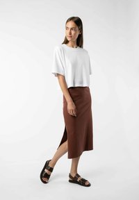 Witte cropped t-shirt gecombineerd met een rustkleurige midi-rok met een zijsplit en bruine sandalen met straps.