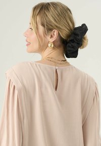 Jasnoróżowa bluzka z teksturowanej tkaniny, z rozcięciem na plecach, plisowanymi rękawami i warstwowym złotym naszyjnikiem. Czarne gumki do włosów.