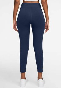 Leggings navy in un tessuto morbido ed elastico con una vita alta e un design aderente, abbinati a scarpe da ginnastica bianche.