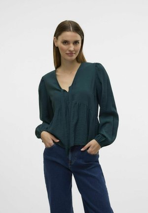 Tegenblauw blouse met een diepe V-hals, pofmouwen, een gestructureerde stof en een geplooid lijfje, gecombineerd met een blauwe spijkerbroek.