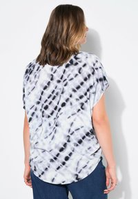 Top corto a maniche corte di vestibilità ampia in un motivo tie-dye bianco e nero. L'orlo curvo aggiunge struttura; tessuto morbido e leggero per il comfort.