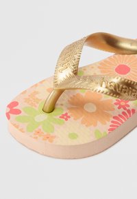 Gold, textured strap flip-flop with a floral patterned footbed in pink, orange, and green. Soft foam sole, slightly curved shape.