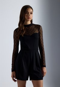 Rompers noirs avec de longues manches transparentes en pois. Le bodice présente un décolleté en cœur et des shorts plissés. Texture lisse dans l'ensemble.