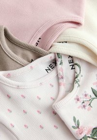 Set of three ribbed tank tops: light pink, beige, and white, with floral prints and small rose patterns. Textured fabric with soft necklines.