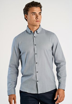 Camicia azzurra chiara con tessuto testurizzato, maniche lunghe e colletto strutturato, caratterizzata da bottoni scuri lungo la parte anteriore.