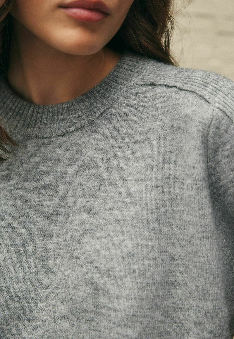 Pull gris en tricot doux, avec un col rond côtelé et une texture subtile. Aucun motif ou accent visible.