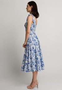 Kwiatowa sukienka midi z dopasowanym topem i rozkloszowanym dołem, z niebieskimi wzorami kwiatowymi na białym tle oraz związanymi ramiączkami.