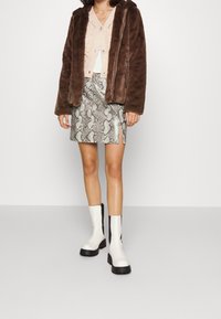 Braune Kunstpelzjacke, hellrosa Strickcardigan, metallic Minirock mit Schlangenprint und weiße Stiefeletten mit schwarzen Akzenten.