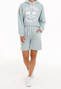 Lichtblauwe katoenen hoodie met witte "California Paradise Life" grafische afbeelding, gecombineerd met bijpassende shorts. Voorzien van trekkoorden en zijzakken.