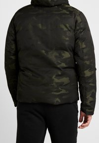 Zielona kurtka ocieplana w kamuflażu z kapturem, gładka w dotyku, z długimi rękawami i wzmocnionymi szwami na ramionach i rękawach.