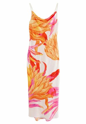 Tânără stă desculță pe o potecă de lemn, purtând o rochie lungă cu imprimeu floral portocaliu și roz, uitându-se în jos.