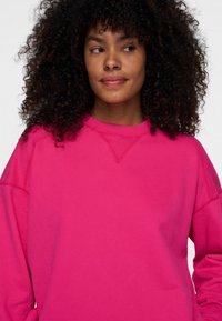 Sudadera fucsia elaborada en suave algodón, con cuello redondo, hombros caídos y puños acanalados. Textura suave con costuras mínimas.