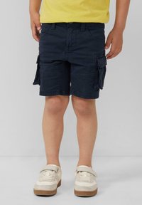 Marine cargoshorts met meerdere zakken, een iets losse pasvorm en van katoen gemaakt. Gecombineerd met beige sneakers met klittenbandsluitingen.