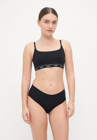 Bralette nera con spalline regolabili e fascia con logo, abbinata a slip neri a vita alta, entrambi realizzati in tessuto liscio e stretch.