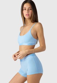 Világoskék bralette és boxer short szett, puha anyagból készült. Vékony pántokkal és márkás derékpántokkal rendelkezik, sima textúrával és letisztult dizájnnal.