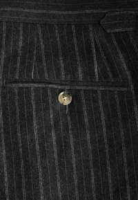 Gray pinstripe fabric features a front pocket with a round, light-colored button. The texture appears soft, with a slightly fuzzy finish.
