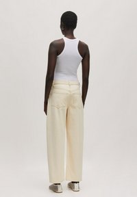 Crèmekleurige wijde jeans met achterzakken, gecombineerd met een witte tanktop en geprinte sneakers. Glad denimtextuur.