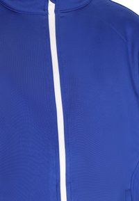 Giacca blu realizzata in tessuto liscio, con una cerniera frontale bianca e un colletto alto. La texture appare leggermente lucida.