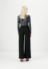 Long-sleeve, fitted top in gray with black leopard print, paired with high-waisted, wide-leg black trousers and black heeled shoes.