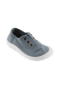 Zapato sin cordones de lona en gris claro con suela de goma blanca, con ojales en tono dorado, punta redondeada y parte superior de tela texturizada.