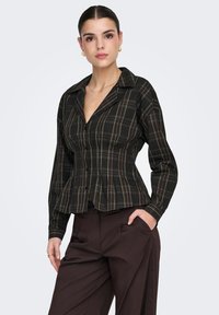 Chemise à carreaux noirs et verts avec col, manches longues et taille cintrée. Présente une fermeture à boutons et un détail de plis subtils.