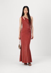 Robe rouge à paillettes, à une épaule, longue, avec une fente sur le côté, silhouette ajustée et détails froncés. Associée à un petit sac doré et des sandales noires.