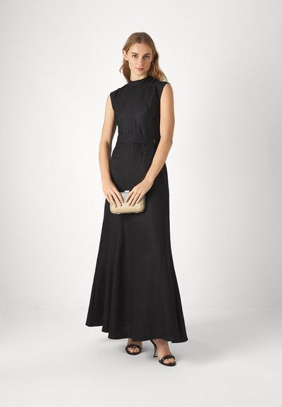 Robe maxi sans manches noire avec un corsage ajusté et une jupe évasée. Portée avec une pochette dorée et des talons à lanières noirs, sur un fond neutre.