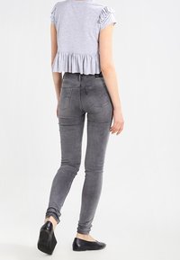 Šedý zkrácený top s volánkovými rukávy, zkombinovaný s přiléhavými šedými džínami a černými balerínami. Hladké textury s pohodlným střihem.