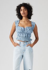 Crop top en coton bleu clair avec smocks élastiques, bretelles volantes et détails en dentelle. Associé à un jean distressed bleu clair à taille haute.