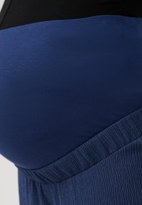 Haut de maternité avec un design bicolore noir et bleu. La section bleue a une texture lisse ; le bas a une finition plissée.