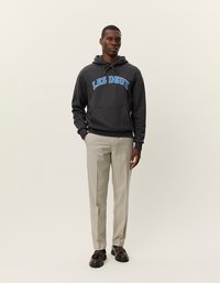 Dunkelgrauer Kapuzenpulli mit "LES DEUX" in blauer Schrift, kombiniert mit hellgrauen, gestreiften Hosen. Das Model steht vor einem neutralen Hintergrund.