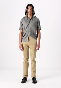 Short-sleeve gray shirt with buttons, tan pants, and black shoes. The fabric appears smooth, and the outfit has a relaxed fit.
