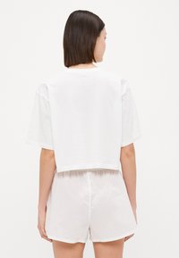 Hvit, kort t-skjorte med korte ermer og rund hals. Kombinert med lyse, elastiske shorts i myk tekstil.