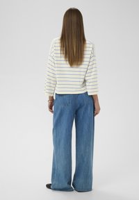 Pull oversize à rayures blanches et bleu clair, associé à un jean en denim bleu à jambes larges. Texture de tissu lisse et coupe décontractée.