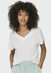 Top blanc à col en V et manches courtes, fabriqué dans un tissu lisse, associé à un pantalon vert clair à taille élastique. Coupe décontractée avec une silhouette relaxée.