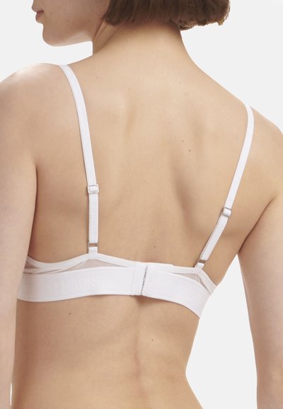 Bílá podprsenka s nastavitelnými ramínky, hladkou texturou látky a elastickou páskou s logem značky. Design je minimalistický a funkční.