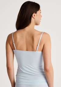 Lichtblauwe camisole met dunne verstelbare spaghettibandjes, aansluitend design en een gladde textuur. De achterkant toont een eenvoudige, minimalistische stijl.