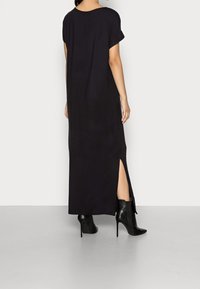 Svart maxiklänning med korta ärmar, sidofå̈ll och en mjuk textur. I kombination med svarta högklackade ankelstövlar.