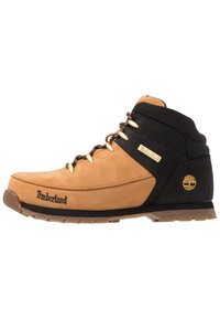 Bota de senderismo de cuero marrón y negro con ojales dorados, cuello acolchado y suela de goma. Presenta el logo de Timberland y acentos texturizados.