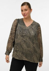 Blouse à manches longues en tissu transparent avec un motif rayé noir et beige ondulé, dotée d'un col en V et d'une coupe décontractée. Pantalons noirs à jambe large.