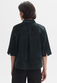 Dark green corduroy shirt with a back pleat, wide sleeves with slits, and a classic collar. Soft texture and a relaxed fit.