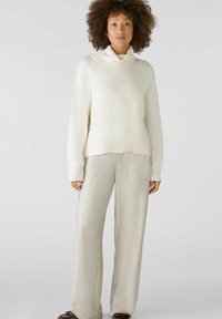 Weißer Rippstrickpullover mit einem Schalkragen, kombiniert mit weit geschnittenen, silbernen Textilhosen. Das Outfit besteht aus sanften, kontrastierenden Materialien.