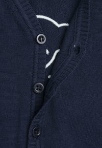 Cardigan bleu marine en tissu tricoté avec un col en V, cinq boutons noirs et un motif de cœurs blancs sur la couche intérieure.