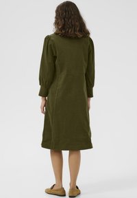 Olive green corduroy dress with a fitted bodice, puffy sleeves, and a knee-length A-line skirt. Features a smooth texture and minimal design.