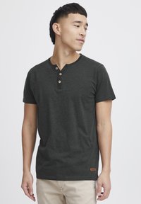 Camiseta henley de manga corta en gris oscuro, fabricada con tejido suave, que cuenta con tres botones de madera en el cuello y una pequeña etiqueta de cuero con la marca en el dobladillo.